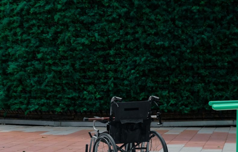 Unoccupied black wheelchair beside a paved path and green hedge