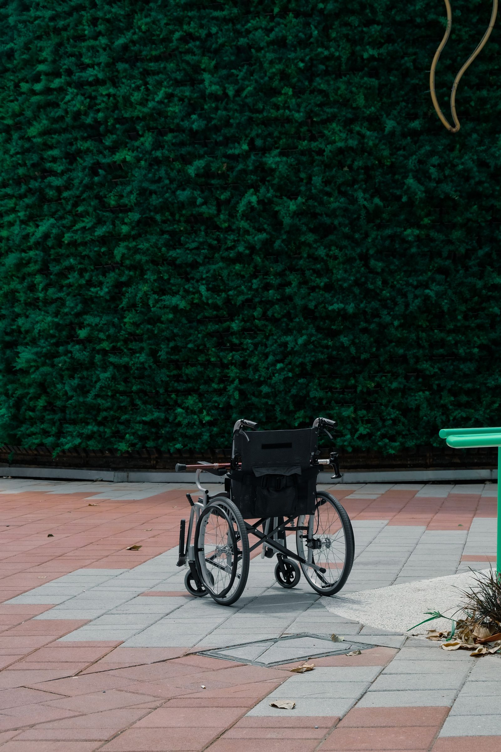 Unoccupied black wheelchair beside a paved path and green hedge